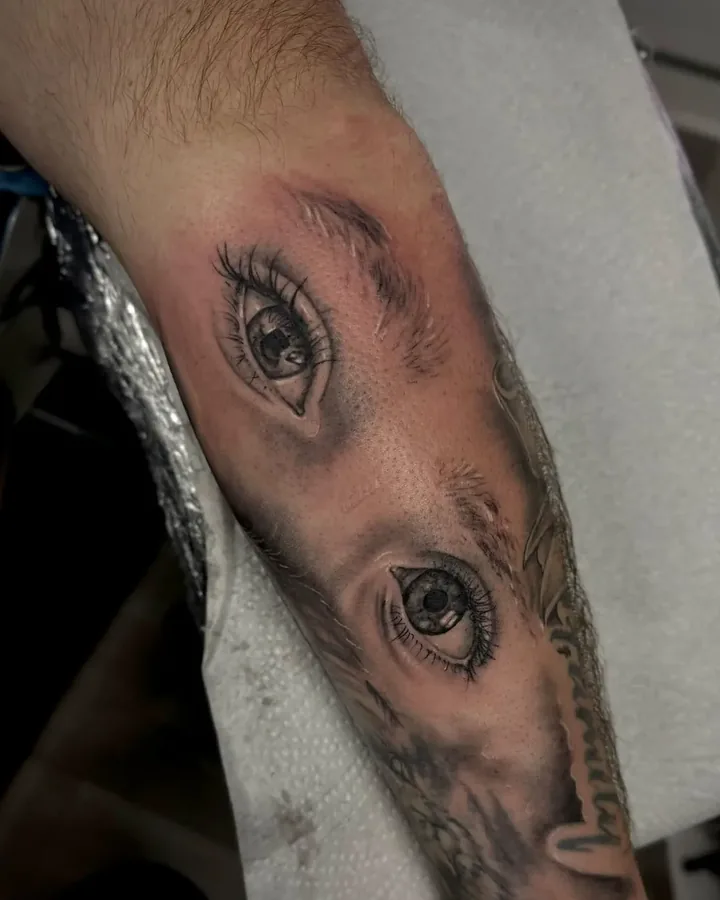 Black and grey realistic pair of eyes with eyebrows, on a forearm